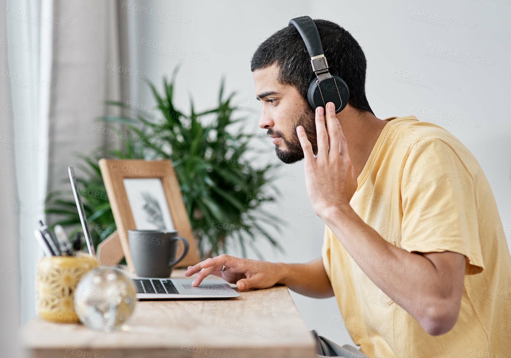 Buy stock photo Shot of a young man using a laptop and headphones while working from home