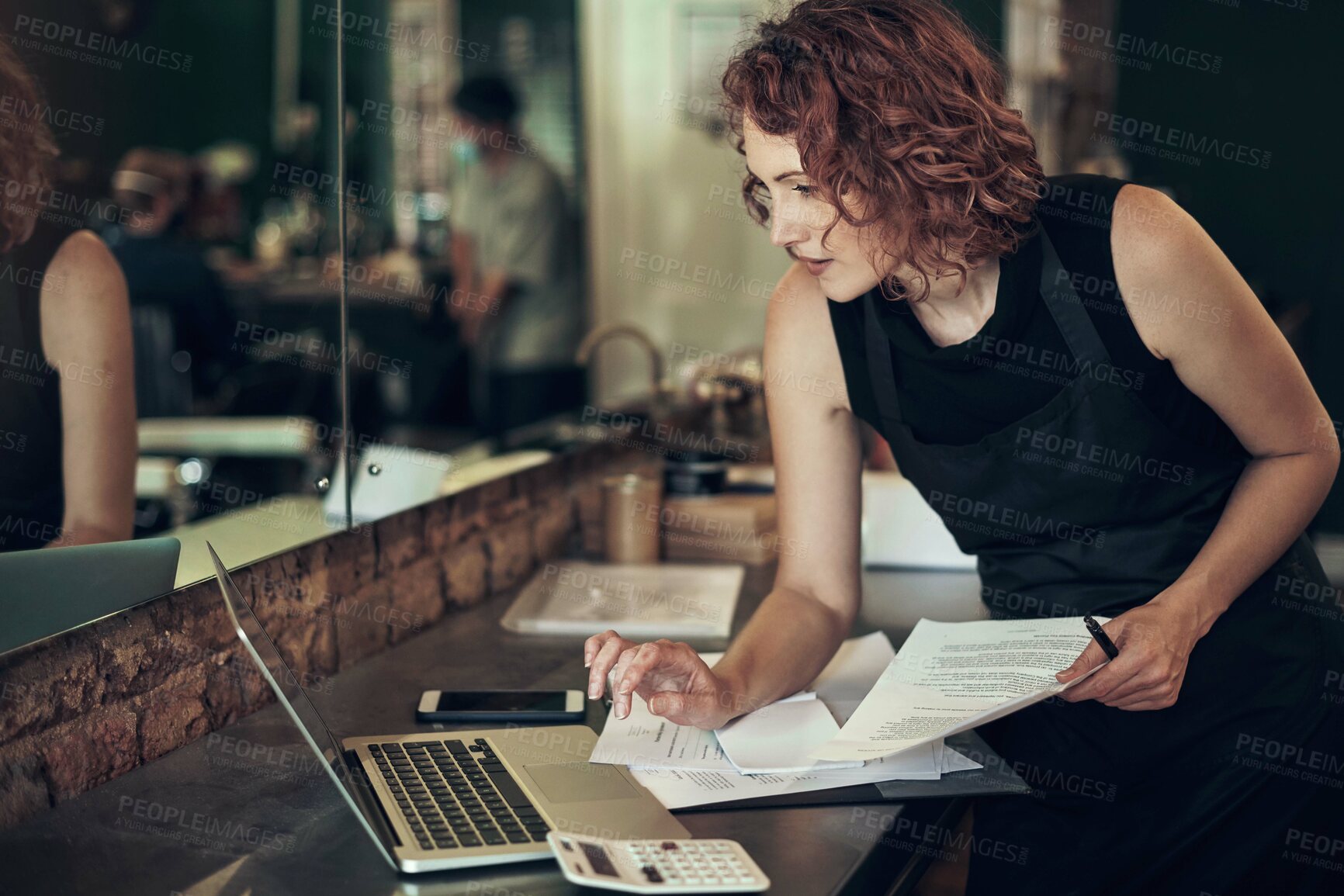 Buy stock photo Shot of an attractive young hairdresser standing and using her laptop while calculating her finances in her salon