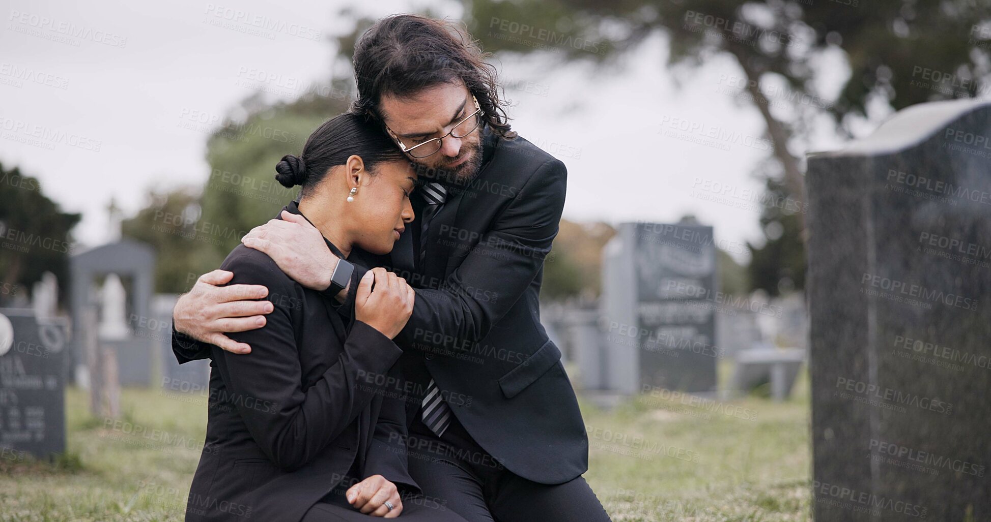 Buy stock photo Sad couple, graveyard and hug in loss, grief or mourning together at funeral, tombstone or cemetery. Man holding woman in comfort, empathy or goodbye at memorial or burial service for death on grass