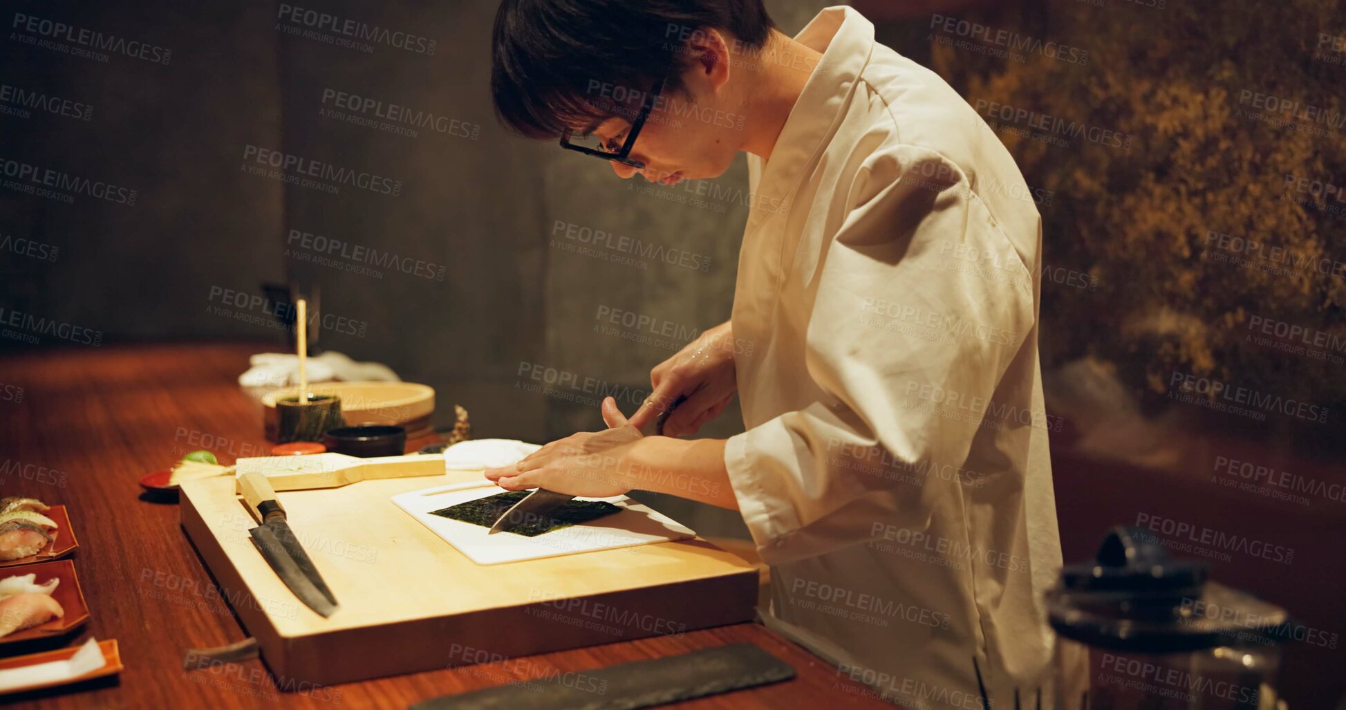 Buy stock photo Japan chef, restaurant and cutting seaweed for sushi, glasses and precision with knife for raw fish in kitchen. Asian man, hands and skill in job on wood board, table and seafood menu for nutrition