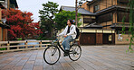 Cycling, travel and man riding by buildings for exercise or transportation to college academy. Fitness, backpack and young male student driving a bicycle to university for carbon footprint by houses.