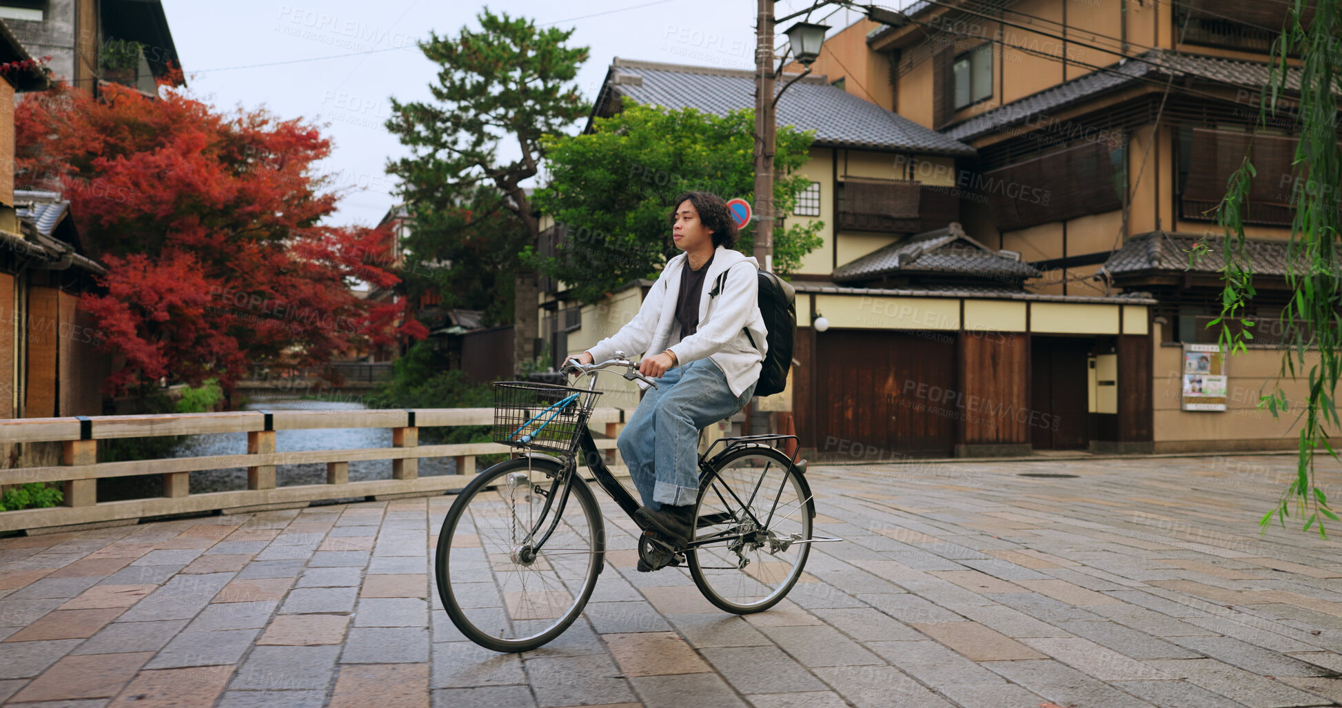 Buy stock photo Cycling, travel and man riding by buildings for exercise or transportation to college academy. Fitness, backpack and young male student driving a bicycle to university for carbon footprint by houses.