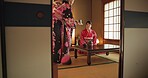Japan, women or matcha tea in kimono for ceremony in Chashitsu room with custom tradition and culture. People, temae and vintage style outfit or dress for heritage, respect or pride with bow on floor