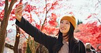 Japanese, woman and selfie in autumn nature with trees, leaves or travel to forest in Kyoto. Red, rainforest and girl smile with smartphone in fall environment with colorful woods and zen garden