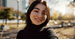 Japanese woman, happy and portrait in park, nature and path with sunshine, city and buildings with pride. Girl, person and smile by lawn, grass and trees in urban metro, outdoor and travel in Tokyo