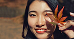 Woman, Asian and face with leaf in autumn, nature and color with happiness outdoor. Environment, plant and smile in portrait, park or garden in Japan with foliage, mockup space and positivity