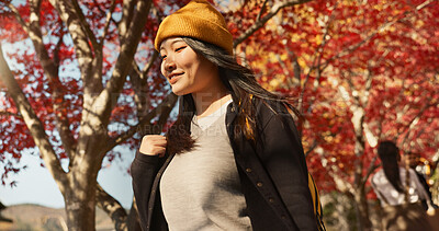 Asian woman, autumn trees and walking in Japan for natural scenery, adventure or journey in nature. Female person smile with backpack or bag for outdoor trip with blooming plants or leaves in season