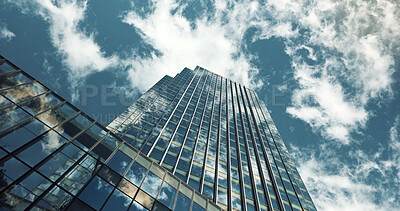 Low angle, skyscraper building and clouds with reflection, nature or urban infrastructure in city. Architecture, cityscape and skyline and metro with landscape, glass and sky background in timelapse