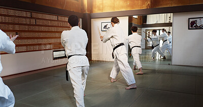 Aikido, group and class with strike, weapon training and wooden sword for self defence exercise. Dojo, students and athlete in a gym or studio with fight challenge, black belt practice and fitness