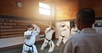 Aikido, group and class with sensei, weapon training and wooden sword for self defence exercise. Dojo, students and athlete in a gym or studio with fight challenge, black belt practice and fitness