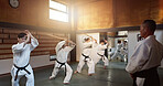 Aikido, group and class with sensei, weapon training and wooden sword for self defence exercise. Dojo, students and athlete in a gym or studio with fight challenge, black belt practice and fitness