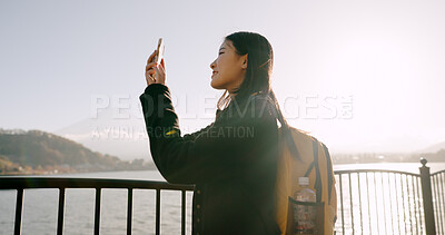 Japanese woman, lake and phone for photography, memory and post on web blog for travel with backpack. Girl, person and outdoor with smartphone by water, river and photoshoot for social media in Tokyo