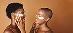 Beauty, eye pads and face of black women in studio with glowing, natural and facial routine. Smile, skincare and portrait of African female friends with cosmetic treatment by brown background.