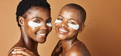 Beauty, eye pads and face of black women in studio with glowing, natural and facial routine. Smile, skincare and portrait of African female friends with cosmetic treatment by brown background.