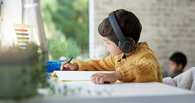 Boy child, homework and writing with headphones, music and focus for learning, drawing or education. Young male kid, notebook and study with audio streaming, radio or listening online in family house