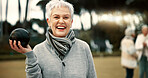 Senior woman, lawn bowling and park with face for sport, fitness or game for competition, health or fun. Elderly lady, metal ball and grass for contest, excited smile or workout in outdoor portrait