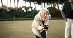 Senior woman, bowling and park on grass for sport, fitness and games for competition, health or fun. Elderly people, metal ball and lawn for contest, funny laugh or workout with blowing for good luck