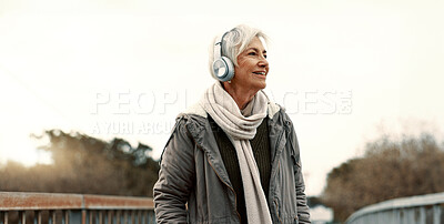 Senior woman, headphones and music outdoor, walking and wellness with audio streaming and energy. Podcast, listen to radio and sound with female person on city bridge, exercise and travel with tech