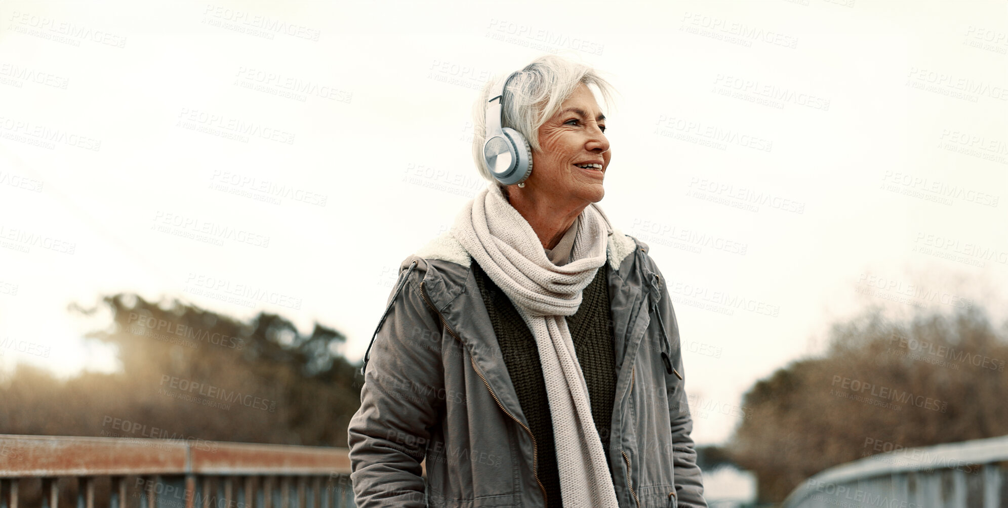 Buy stock photo Senior woman, headphones and music outdoor, walking and wellness with audio streaming and energy. Podcast, listen to radio and sound with female person on city bridge, exercise and travel with tech
