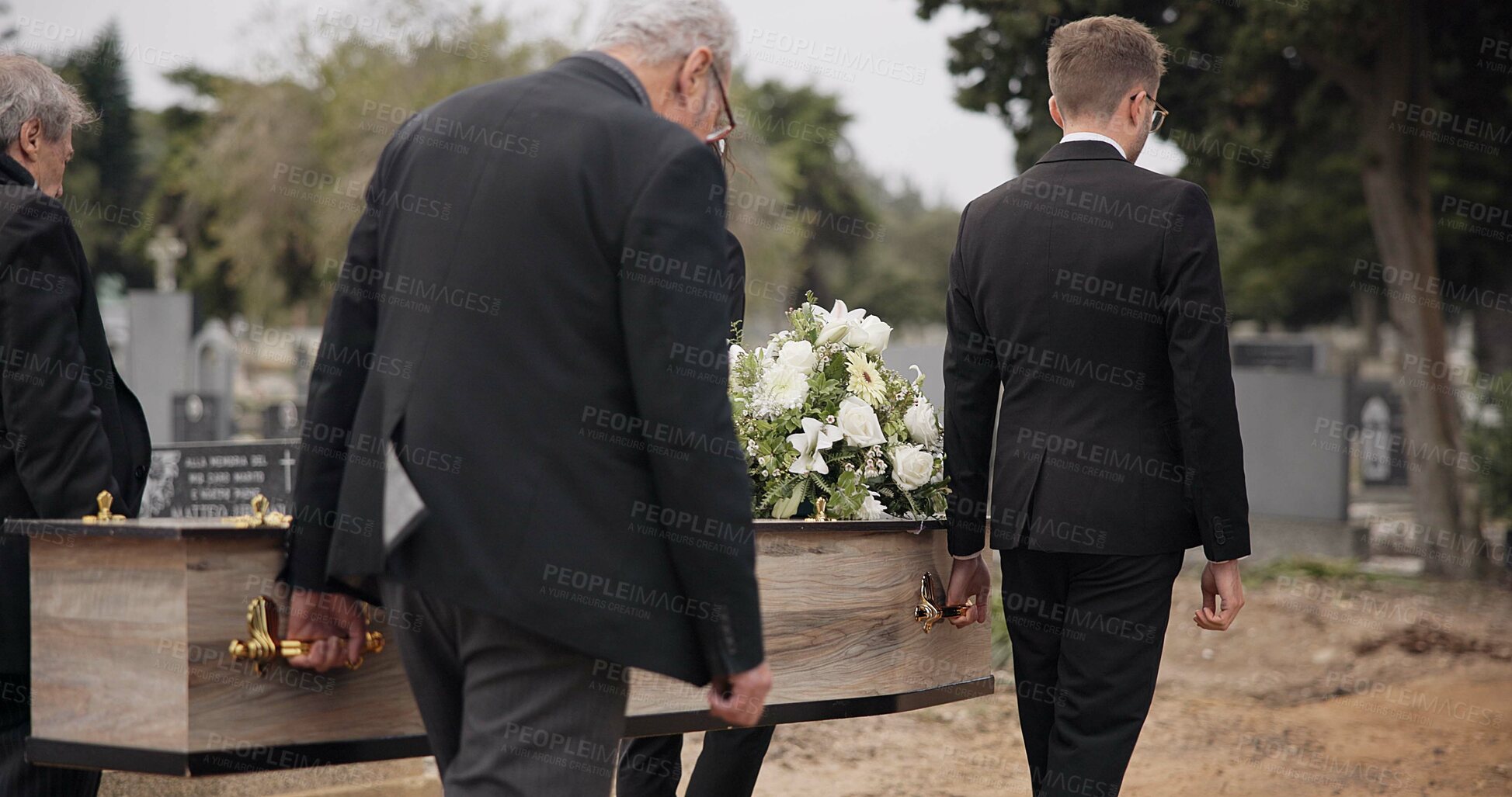 Buy stock photo Coffin, men and pallbearers walking at graveyard ceremony outdoor at burial tomb. Death, grief and group casket at cemetery, carrying to funeral and family service of people mourning at windy event