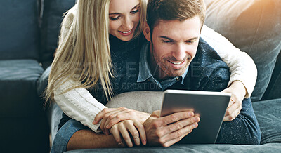 Buy stock photo Cropped shot of an affectionate young couple using a digital tablet while lying on their sofa at home