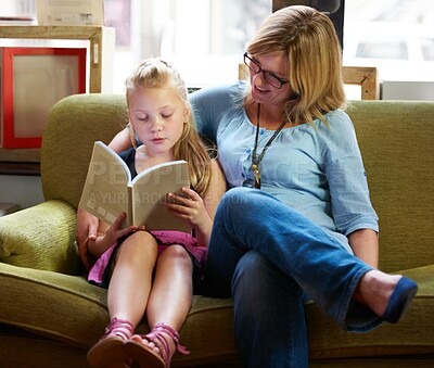 Buy stock photo A cute blonde girl and her mother reading on the couch at home
