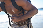 Black man, backpack and fitness on beach for workout, exercise or outdoor cardio by the ocean coast. Closeup of muscular African male person running with bag for adventure by the sea in nature