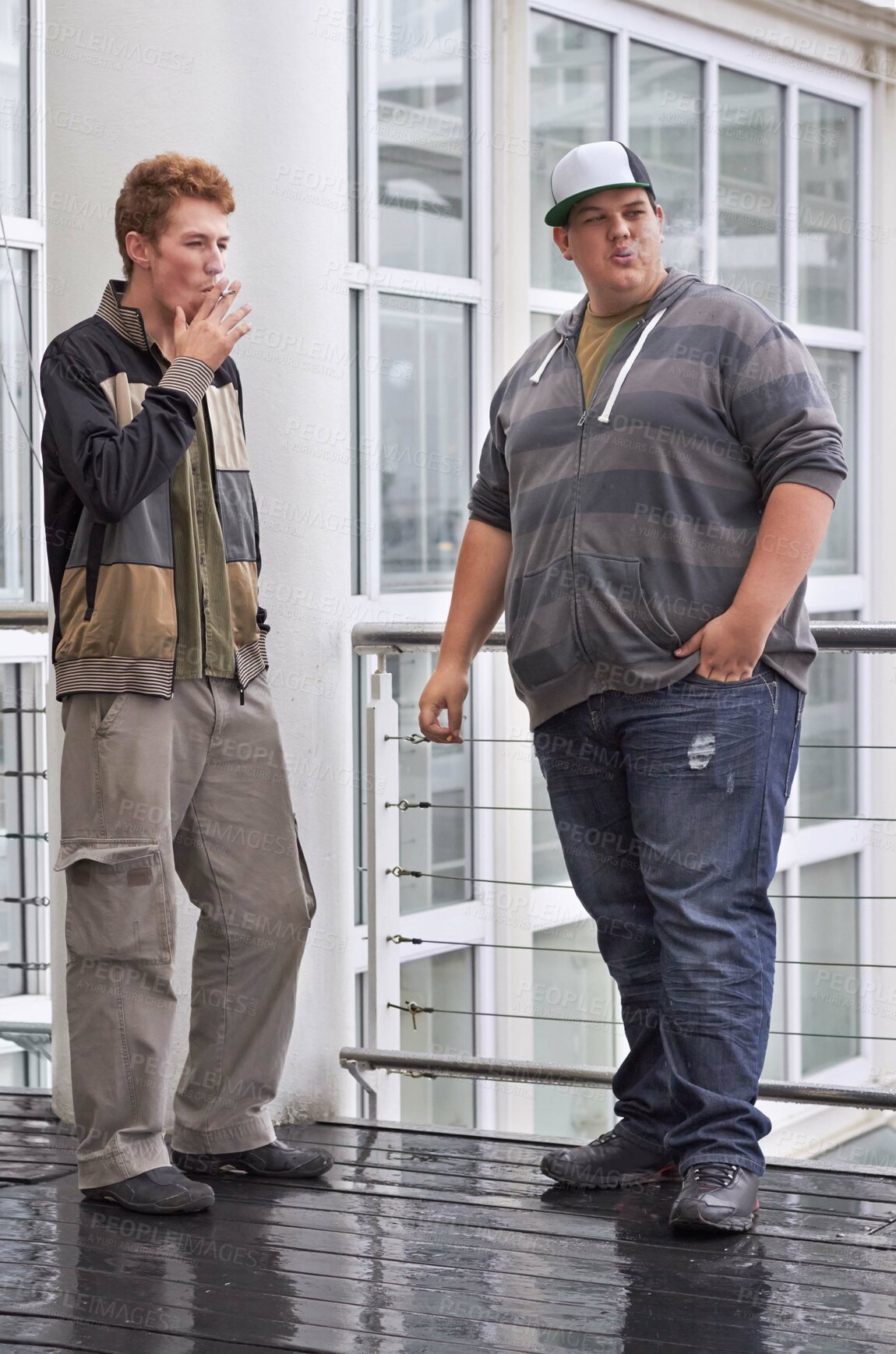 Buy stock photo Teen men, friends and smoking outside education and school building outdoor. Rebel, guys and teenager students with tobacco and cigarette smoke in the rain with a male young friend of university