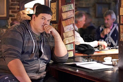 Buy stock photo Man portrait, pub and plus size person waiting for a alcohol and beer drink looking serious. Male person, restaurant and alcoholic sitting at a counter at a club with gen z, cool and urban fashion 