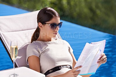 Buy stock photo An attractive young woman reading a magazine while lying on a deck chair