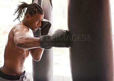 Buy stock photo Shot of a young boxer practicing on a punching bag in a gym