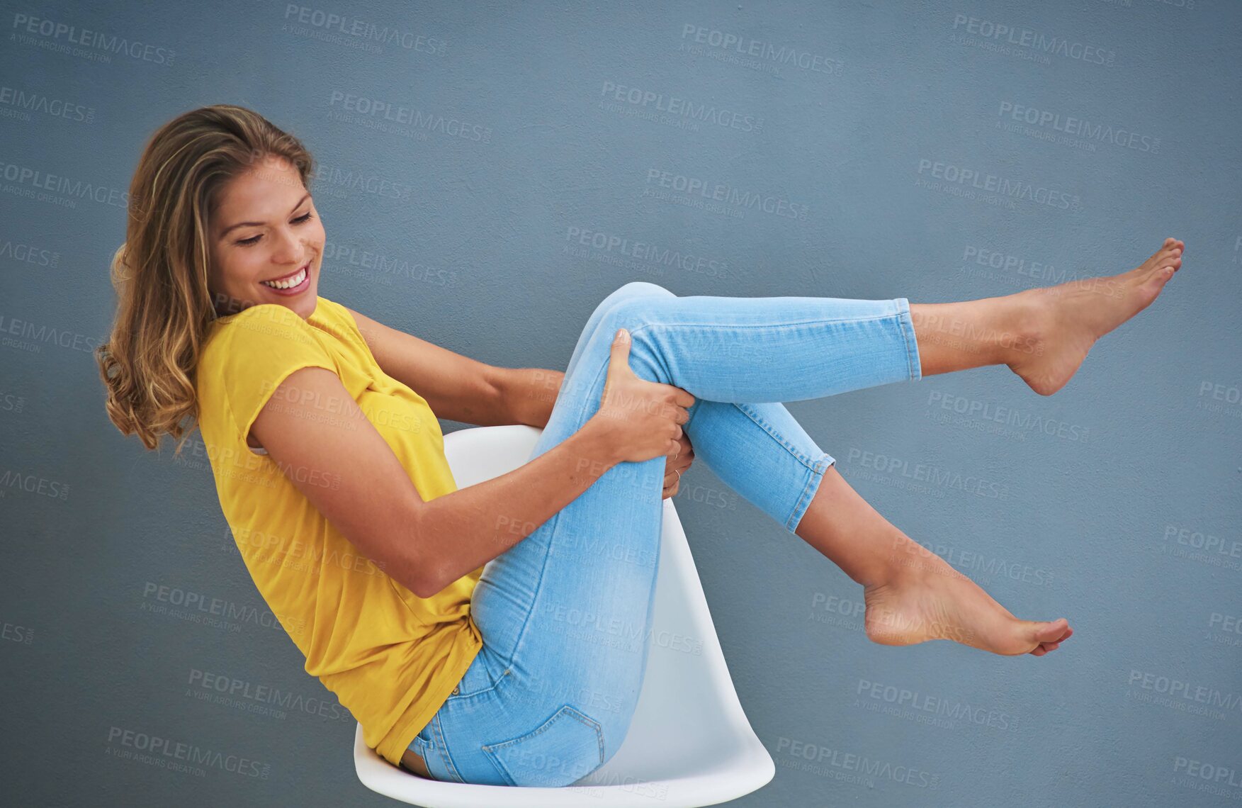 Buy stock photo Shot of a young woman sitting on a chair against a gray wall