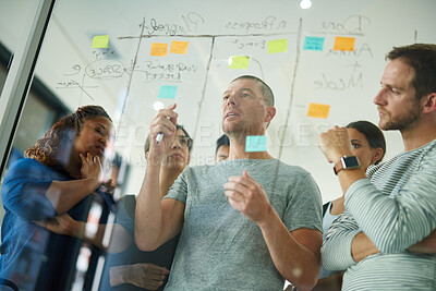 Buy stock photo Business people brainstorming, planning and thinking of ideas on a glass board. A group or team of young professional designers using sticky notes to organize their thoughts in a modern office.