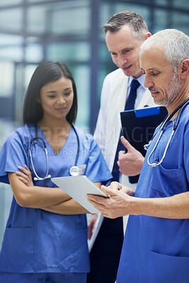 Buy stock photo Shot of a group of doctors talking together over a digital tablet while standing in a hospital