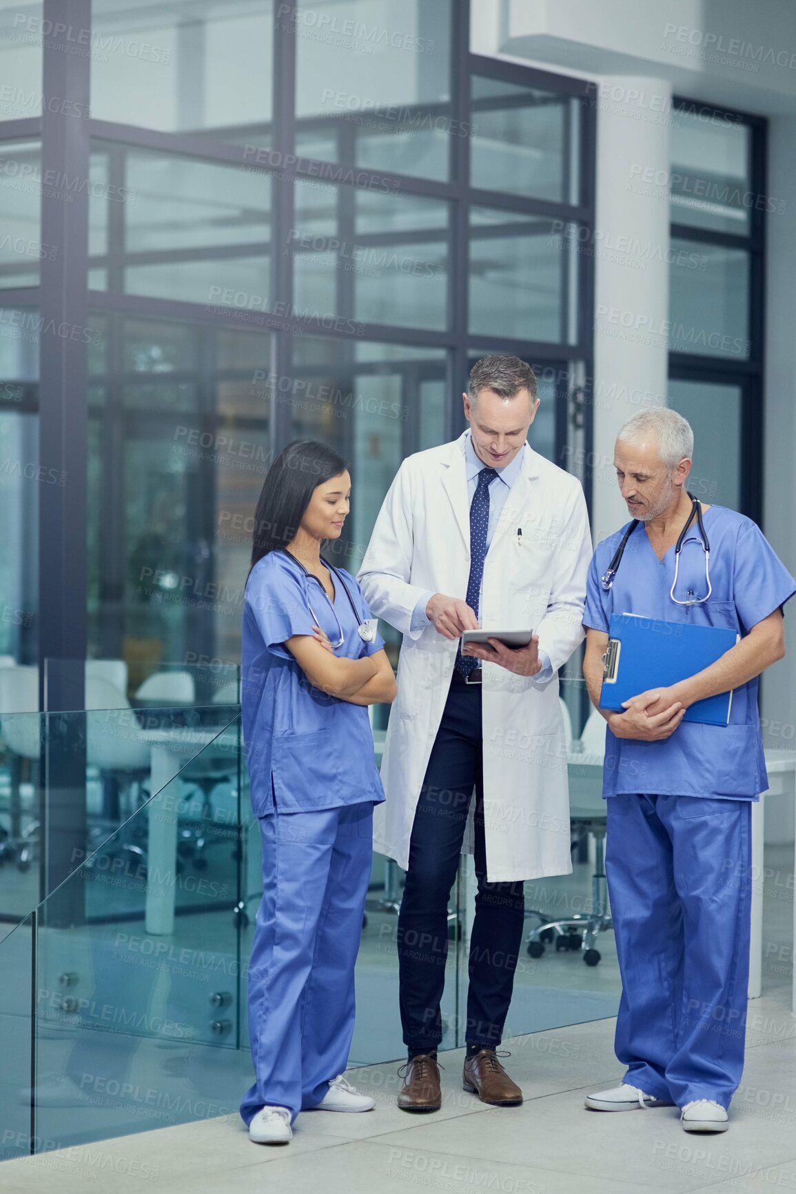 Buy stock photo Shot of a group of doctors talking together over a digital tablet while standing in a hospital