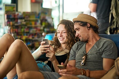 Buy stock photo Shot of a young tourist couple checking their phones while relaxing in a cafe