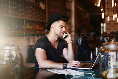 Buy stock photo Shot of a young man using a phone and laptop while working in a coffee shop