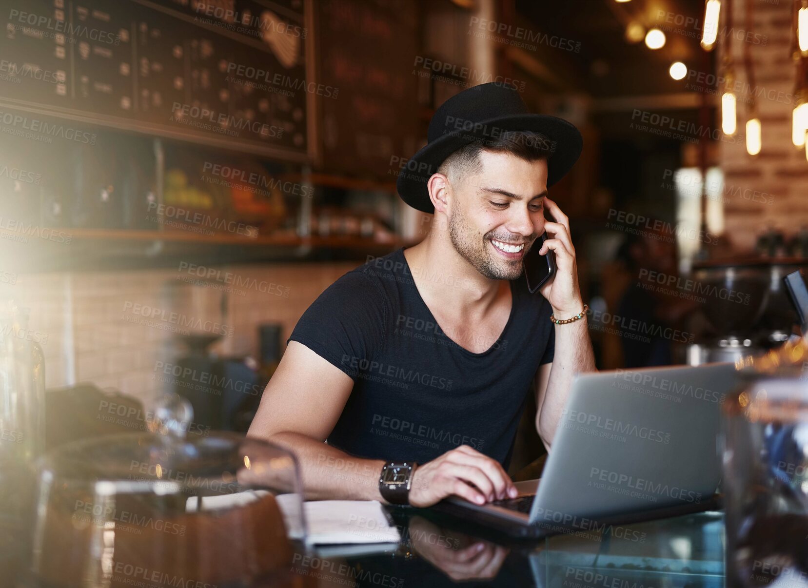 Buy stock photo Shot of a young man using a phone and laptop while working in a coffee shop