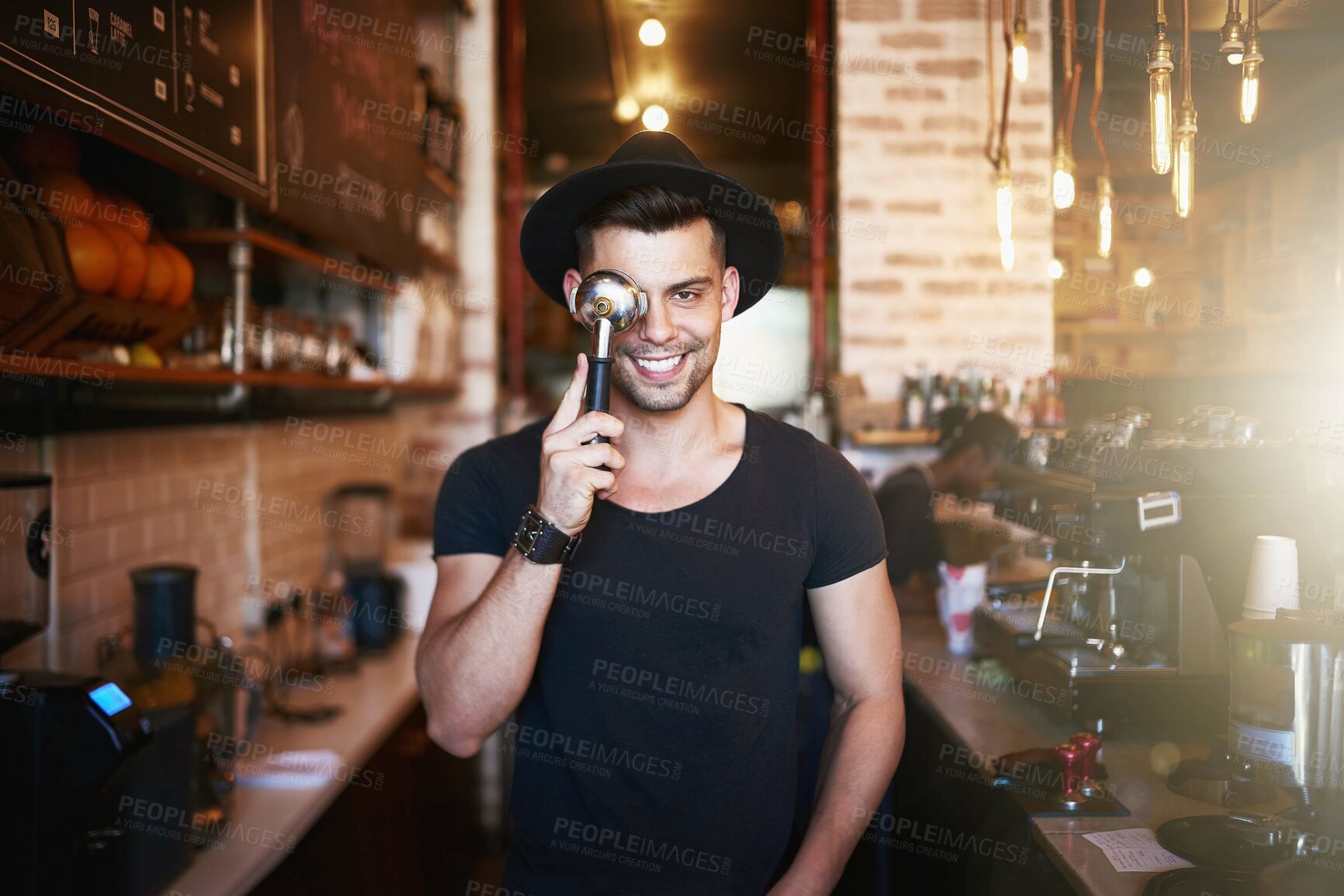 Buy stock photo Shot of a young man covering his eye with a coffee filter while working in a cafe