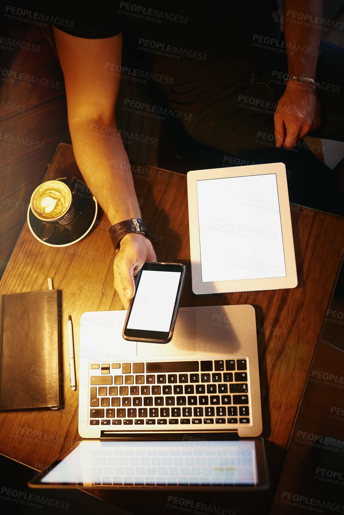 Buy stock photo Cropped high angle shot of a man using a phone and laptop while working in a coffee shop