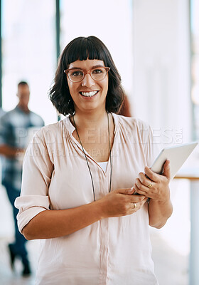 Buy stock photo Portrait of a young woman holding a digital tablet in a modern office with her colleagues in the background