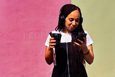 Buy stock photo Cropped shot of an attractive young woman standing against a pink wall and using technology while holding a takeaway coffee
