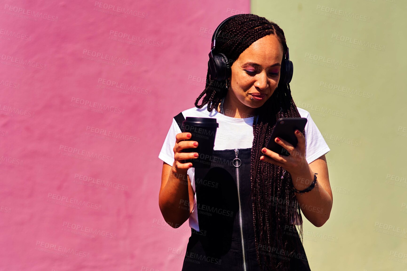 Buy stock photo Cropped shot of an attractive young woman standing against a pink wall and using technology while holding a takeaway coffee