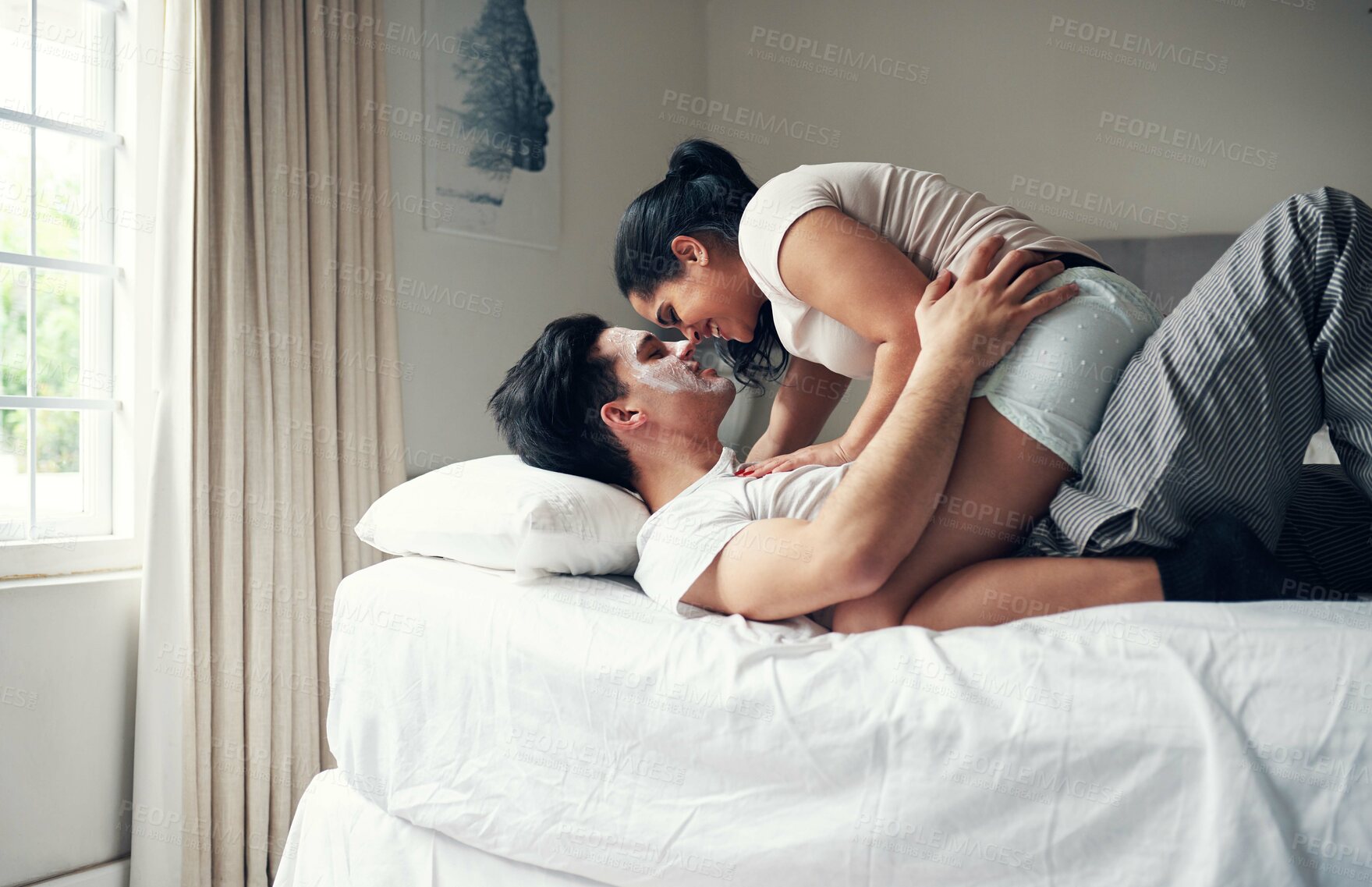 Buy stock photo Shot of a young man wearing a facial mask while lying on his bed with his girlfriend sitting on top of him