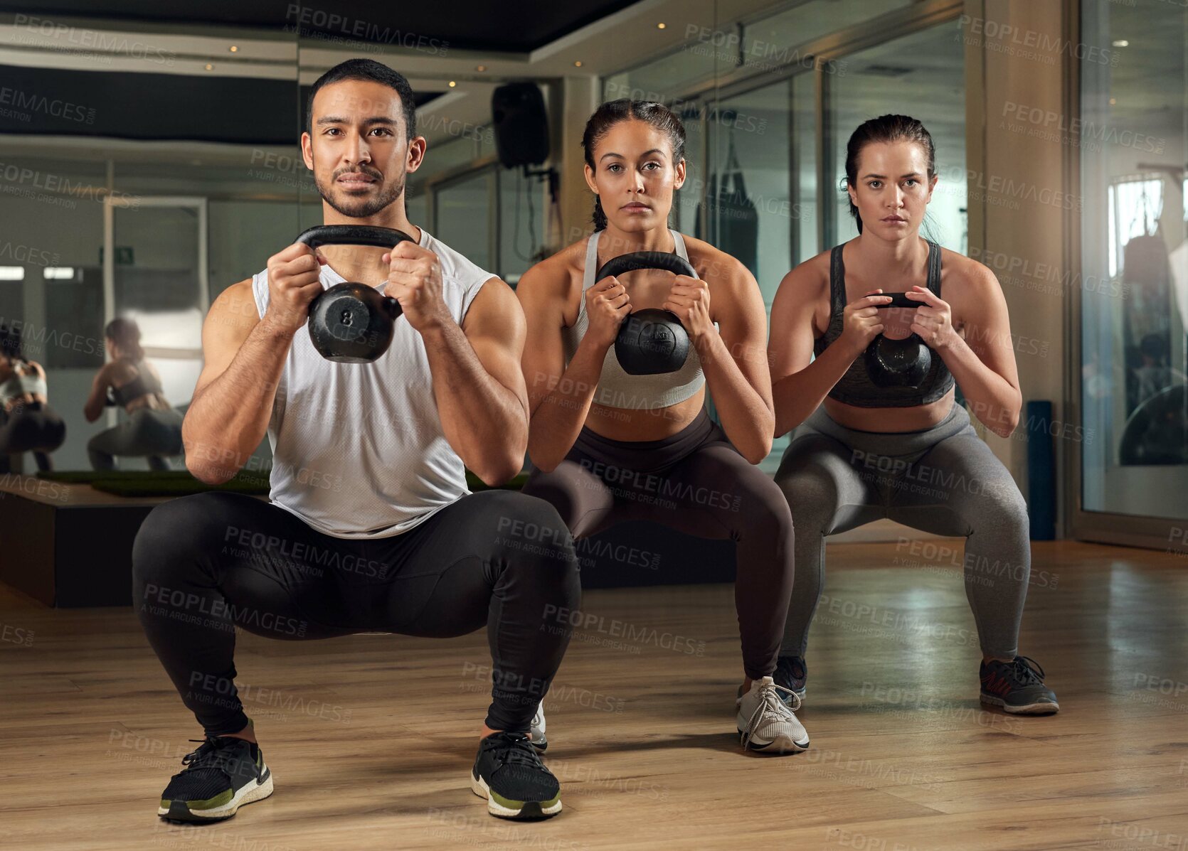 Buy stock photo Full length portrait of three young athletes working out with kettle bells in the gym