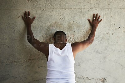 Buy stock photo Rearview shot of a man leaning against an urban wall with his hands up