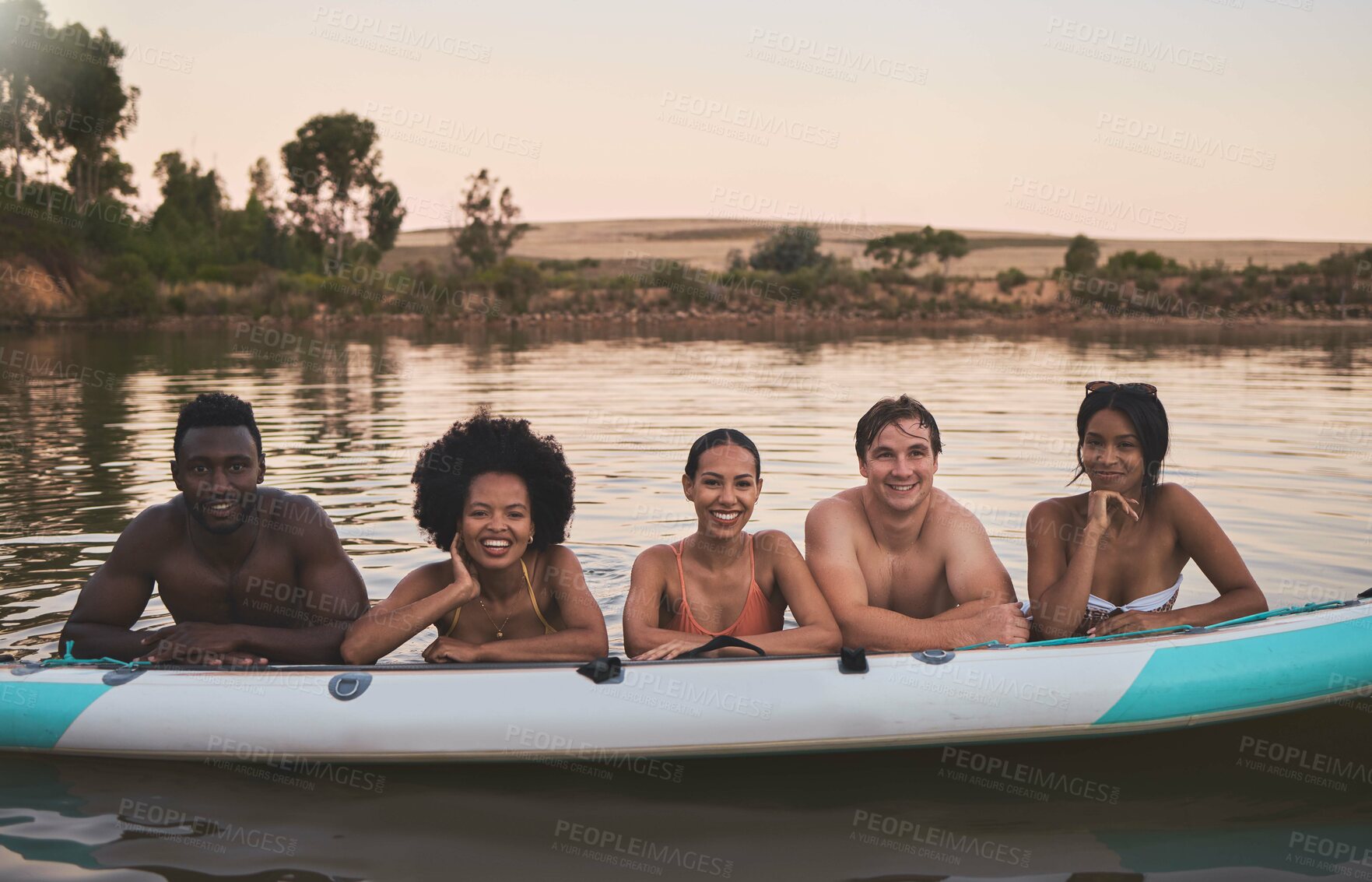 Buy stock photo Diverse group of friends having fun while swimming at a lake in summer with a floating kayak boat. Happy, young and multiracial people on vacation enjoying nature and water on a canoe at sunset.