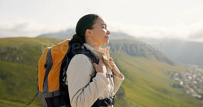 Young woman, trekking on mountains and breathing fresh air for outdoor wellness, fitness and health. Happy person in wind with backpack and hiking in nature on a hill for adventure, travel or journey