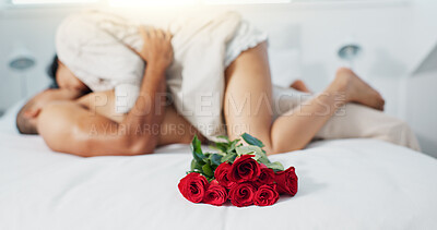 Couple, red roses and lying on bed for anniversary, love or valentines day in romance, embrace or trust at home. Romantic man and woman in bedroom intimacy, passion or bonding with flowers at house