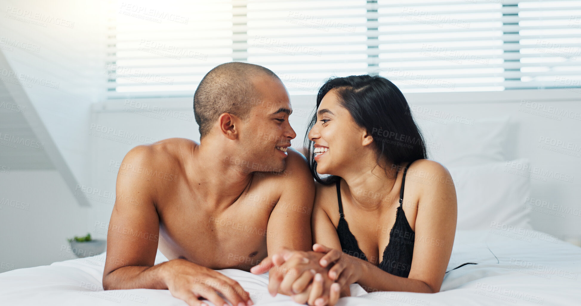 Buy stock photo Happy couple, relax and kissing on bed for affection, morning romance or love in embrace, trust or care at home. Young man and woman smile lying in bedroom for intimacy, passion or bonding at house